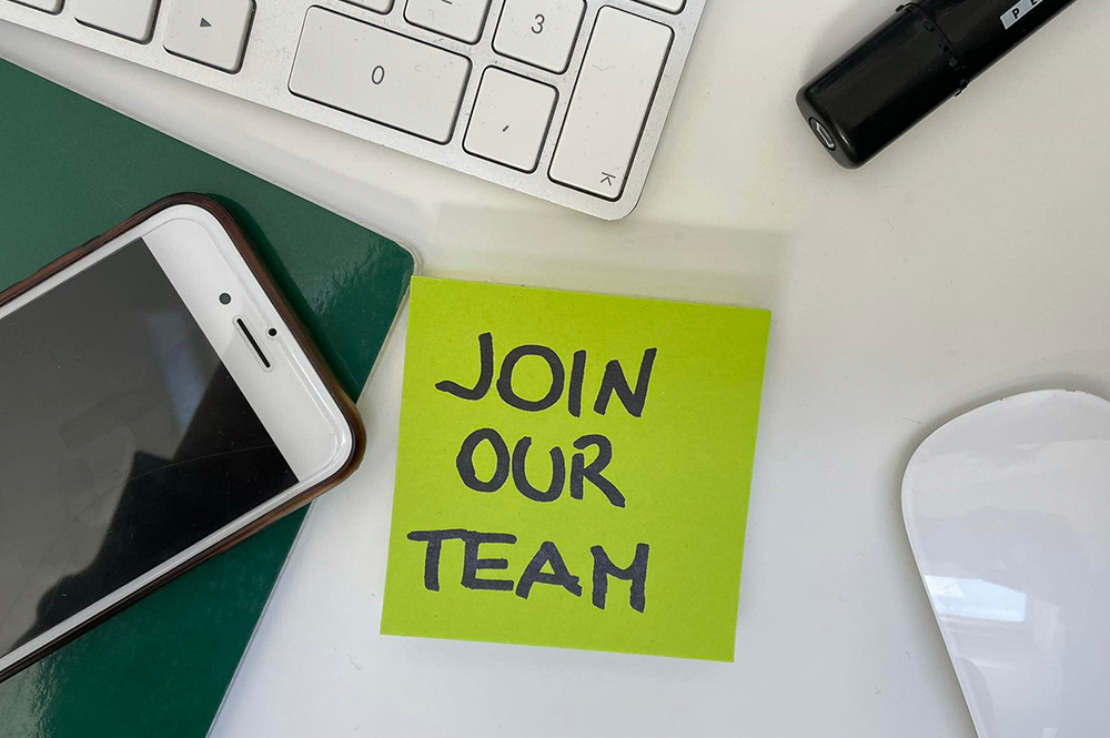 sulla scrivania c'è un quaderno, un telefono un mouse e un post it con scritto "Join our team"
