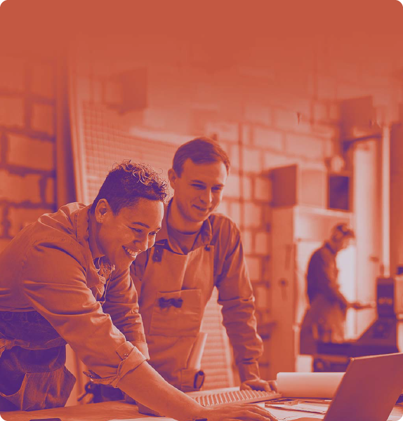 foto con sfondo sull'arancione con con due uomini vestiti da lavoro, appoggiati ad un tavolo che stanno guardando un pc e sorridono