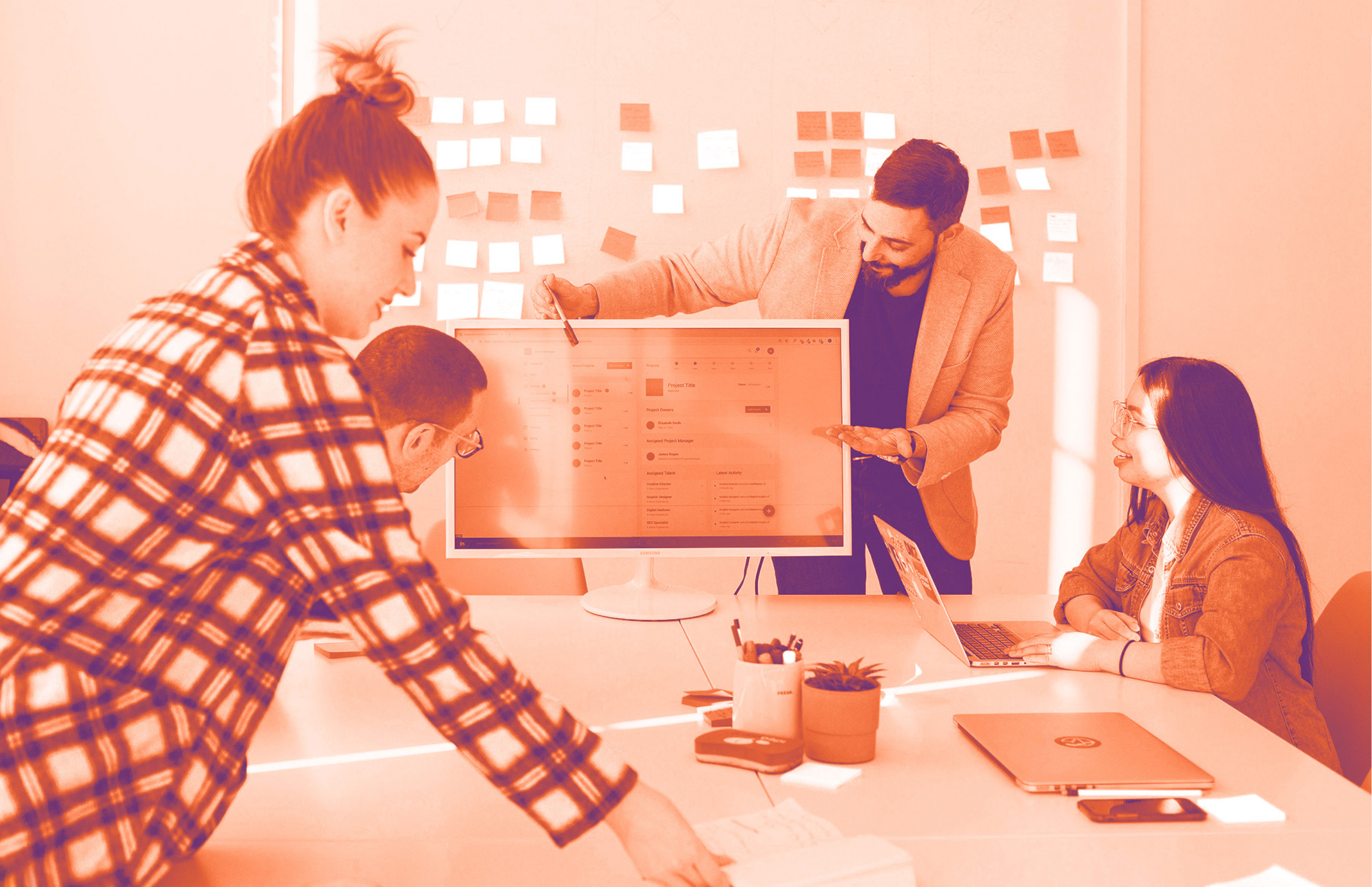 foto con gradiente arancione con delle persone attorno alla scrivania che scambiano opinioni guardando un lavoro al pc