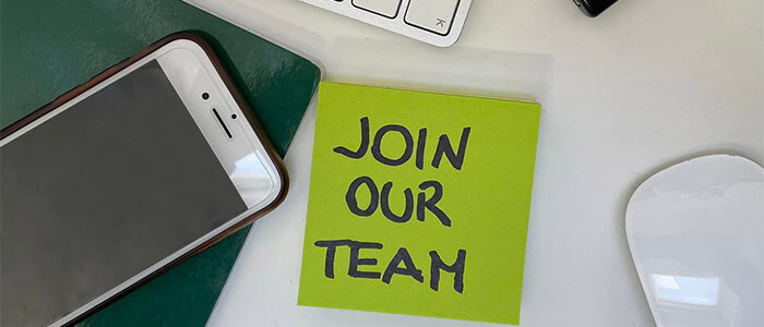 sulla scrivania c'è un quaderno, un telefono un mouse e un post it con scritto "Join our team"